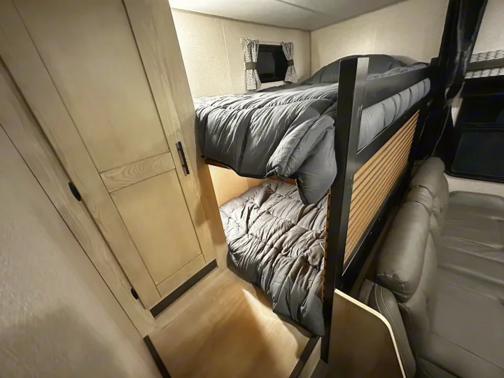 Cozy RV rental interior featuring bunk beds with grey comforters, a compact sofa, and light wood cabinetry.. Connect SE 2022