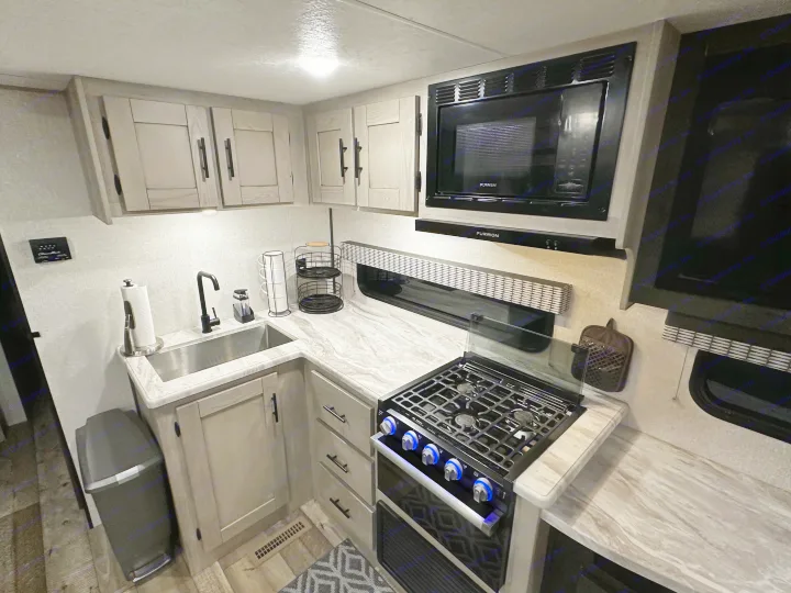 Explore a modern RV rental kitchen featuring light wood cabinets, marbled countertops, a sink, stove, and microwave.. Connect SE 2022