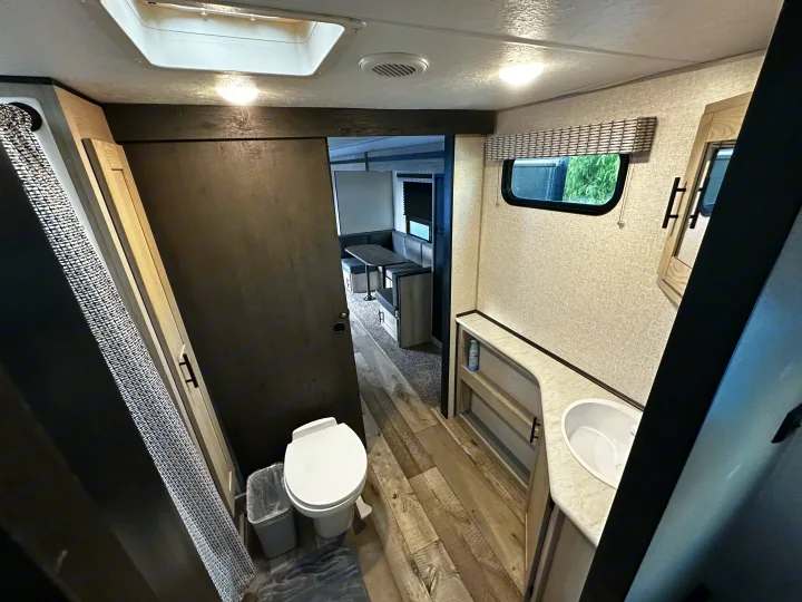 RV rental interior: Clean bathroom with toilet, sink, and shower; view of dinette. Ideal for your next journey.. Connect SE 2022