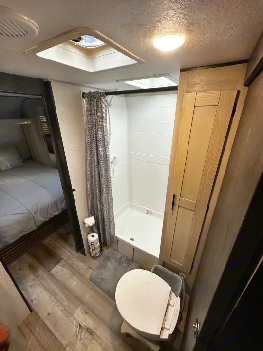 Compact RV rental interior featuring a functional bathroom with shower & toilet, plus a peek into the cozy bedroom.. Connect SE 2022