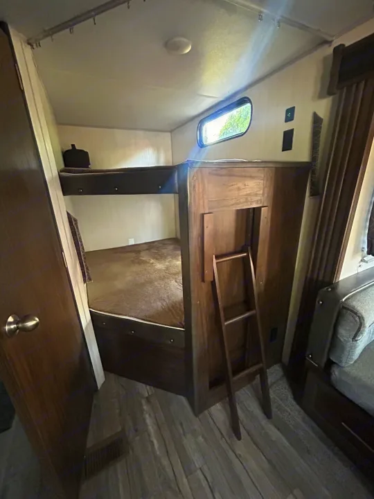 Comfortable bunk beds with a ladder in an RV rental, featuring wood-look flooring and a small window.. Forest River Cherokee Grey Wolf 2019