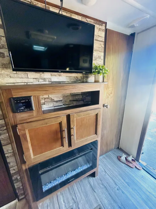 Cozy RV rental living space featuring a TV, Furrion stereo, electric fireplace, and small plant. Slippers by the door.. Forest River Cherokee Grey Wolf 2019