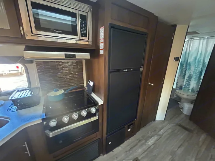 Step inside this RV rental kitchen! Features a microwave, stove, fridge, and glimpse of the bathroom.. Forest River Cherokee Grey Wolf 2019