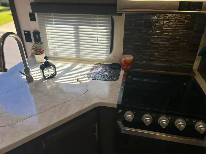 This RV rental kitchen features a modern sink, stovetop, and window with blinds. Bright, compact, and ready for your travels.. Forest River Cherokee Grey Wolf 2019
