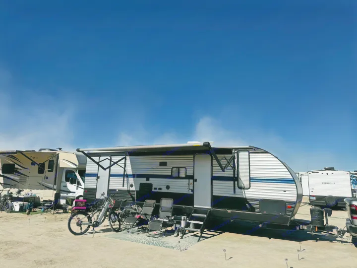 An RV rental travel trailer setup, with bicycles and chairs, at a sunny outdoor camping site with other RVs.. Forest River Cherokee Grey Wolf 2019