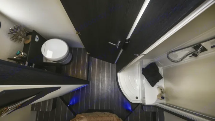 Compact RV rental bathroom: overhead view showing a toilet, corner shower, and dark wood-look floor. Efficient design.. Roller Team 696 2024