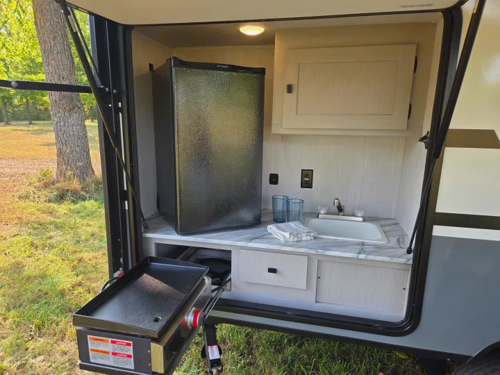 This rv rental's outdoor kitchen provides a fridge, sink, cabinets, and a pull-out griddle, great for camping meals.. Coachmen Apex Nano 2024