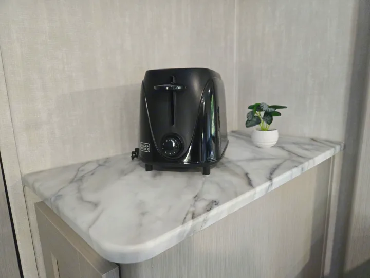 Convenient black toaster and small plant on a marble countertop inside a clean rv rental kitchen area.. Coachmen Apex Nano 2024