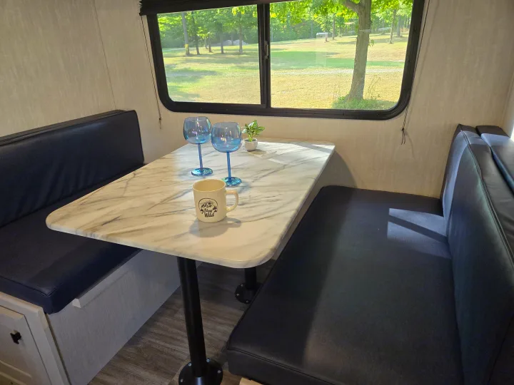 RV rental dinette: comfy benches, marble table with blue goblets & mug, plus a beautiful scenic view.. Coachmen Apex Nano 2024