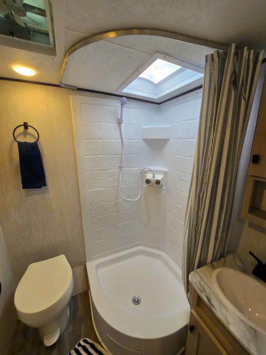 RV rental bathroom with a compact corner shower, toilet, and vanity sink. A skylight brightens this efficient space.. Coachmen Apex Nano 2024