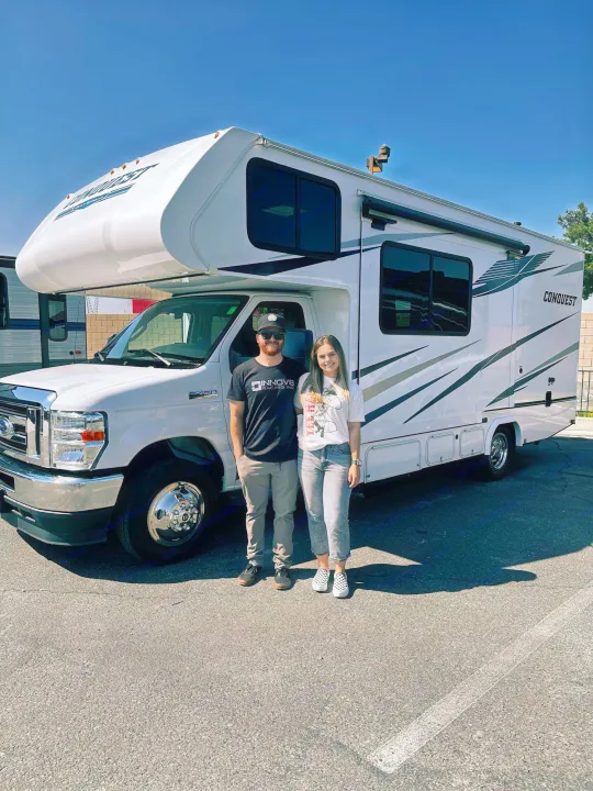 Happy couple with their bright white Gulf Stream Conquest Class C RV rental, a Ford E-450, ready for adventure.. Gulf Stream Conquest 2023