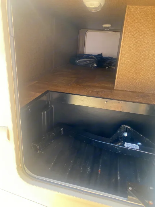 Spacious RV rental storage compartment with a black hitch, bundled items, tiled floor, and overhead lights.. Thor Axis 2016
