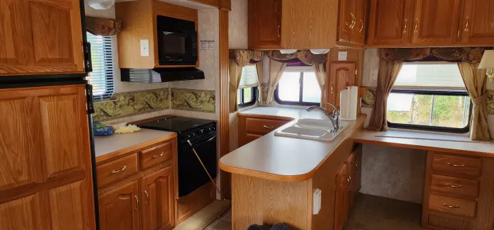 Spacious RV rental kitchen featuring light wood cabinets, fridge, stove, microwave, and a bright sink area.. Keystone RV Montana 2004