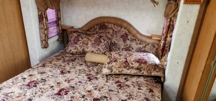 Discover comfort in this cozy RV rental bedroom: floral bed, padded headboard with shelves, and window with blinds.. Keystone RV Montana 2004