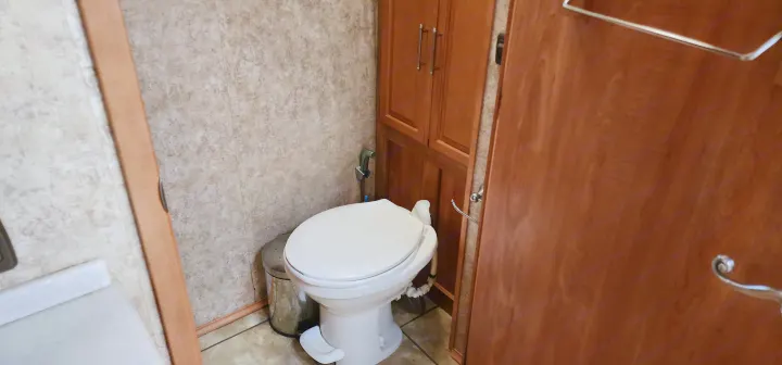 This RV rental bathroom features a white toilet with a bidet sprayer, adjacent cabinet storage, and a small trash can.. Winnebago Journey 2006