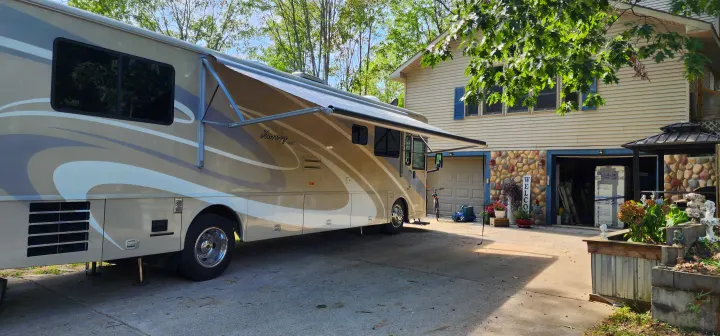 A large, light-colored motorhome, ideal for an RV rental, is parked with its awning extended beside a house.. Winnebago Journey 2006