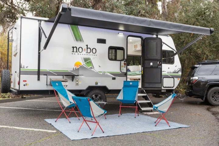 This RV rental, parked with an SUV, boasts an extended awning, blue chairs, and a grill for comfortable outdoor living.. No Boundaries 19 2023