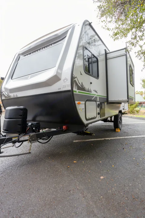 Low-angle view of a "No Boundaries" travel trailer RV, ideal for an RV rental. Features include a side slide-out and nature graphics.. No Boundaries 19 2023