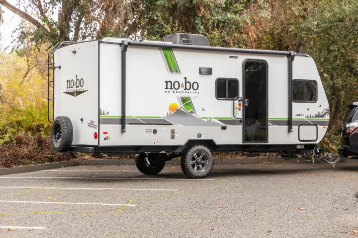 White no bo travel trailer RV, an ideal rv rental, showcasing rugged tires, rear ladder, and nature graphics for outdoor adventures.. No Boundaries 19 2023