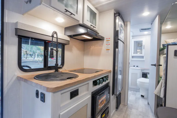 Cozy RV rental interior: modern kitchen with sink, stove, fridge, and view of bathroom and bunk beds.. No Boundaries 19 2023