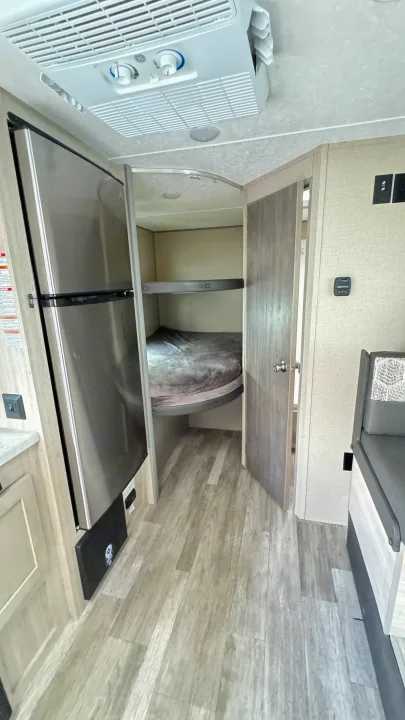 An RV rental interior featuring bunk beds, a stainless steel refrigerator, and a dinette. Overhead AC unit and wood-look flooring.. Coachmen Catalina 2023