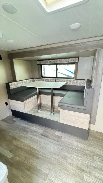 RV rental: Cozy U-shaped dinette with dark grey booth seating, a light wood-grain table, and patterned cushions on wood-look flooring.. Coachmen Catalina 2023
