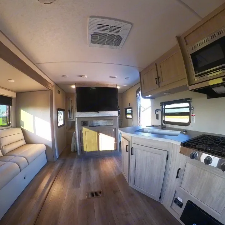 Bright RV rental interior featuring a modern kitchen with stove/sink, comfy couch, and large TV.. Coachmen Catalina 2024