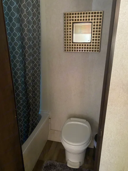 Compact RV rental bathroom with toilet, tub, and patterned shower curtain. A mirror hangs above the toilet.. Starcraft Autumn Ridge 2018
