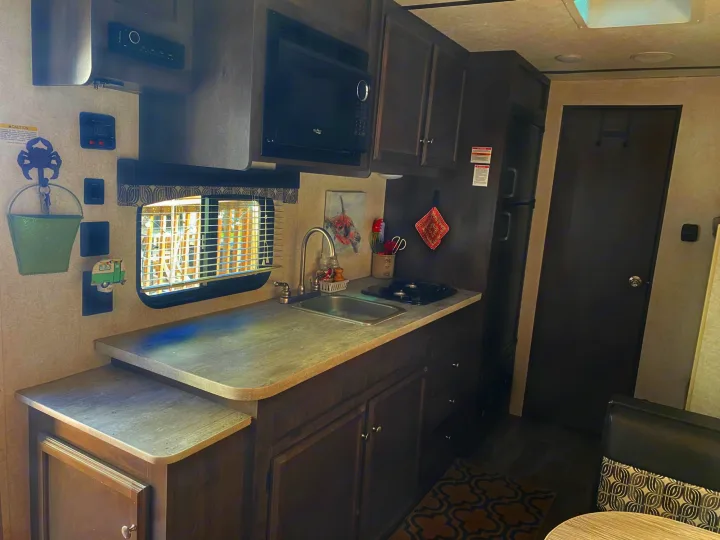 Compact RV rental kitchen area features a sink, stove, microwave, fridge, and ample storage for mobile living.. Starcraft Autumn Ridge 2018