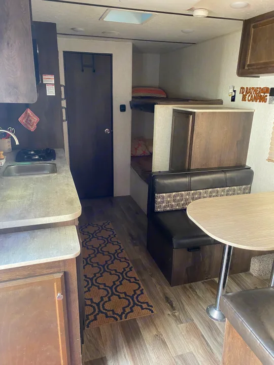 RV rental interior: Equipped with a kitchen, dining booth featuring patterned cushions, and bunk beds. Wood-look flooring is visible.. Starcraft Autumn Ridge 2018