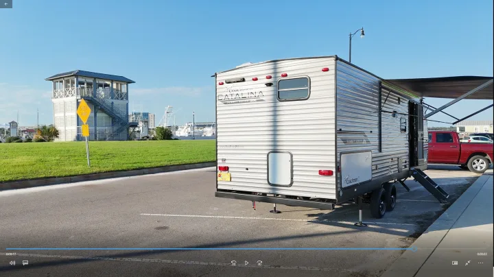 This RV rental, a grey travel trailer with its awning out and steps down, is parked by a marina tower.. Coachmen Catalina 2024