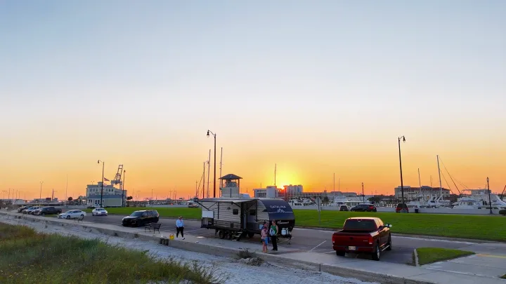 Experience travel! An RV rental is parked by boats at a marina, bathed in beautiful sunset light with people nearby.. Coachmen Catalina 2024