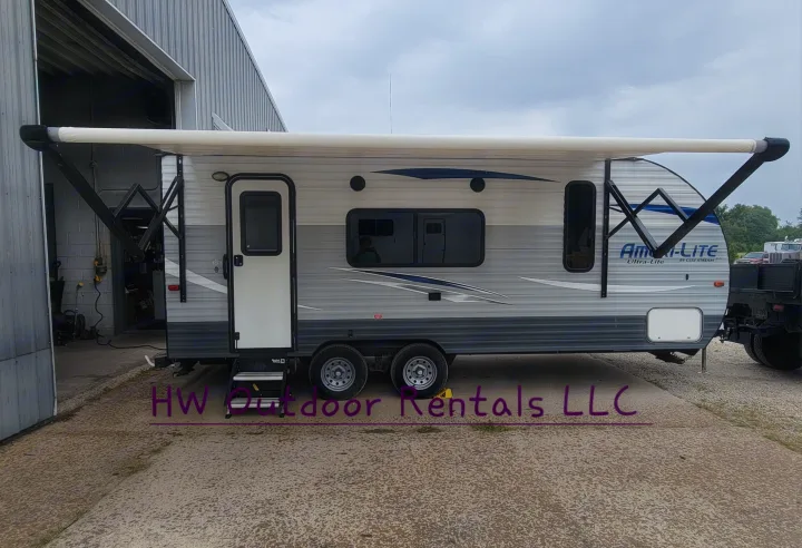Travel trailer RV rental with white awning extended, ready for adventure. Parked outside a building on concrete.. Gulf Stream Ameri-Lite 2018
