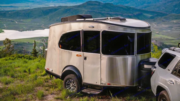 This RV rental makes adventuring easy! A sleek travel trailer & SUV parked on a scenic mountain by a lake.. Airstream Basecamp 2021