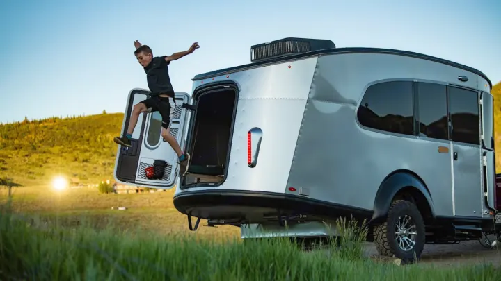 Boy leaping from a silver travel trailer, capturing the joy of an RV rental and outdoor adventure.. Airstream Basecamp 2021