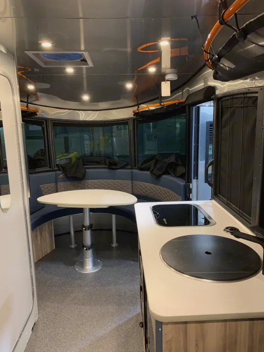 This bright RV rental interior offers a dining area, practical kitchen, and ample overhead storage for your journey.. Airstream Basecamp 2021
