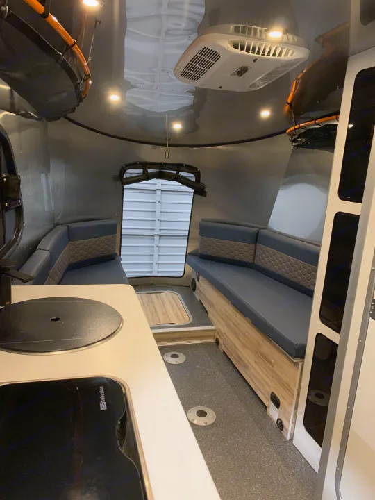 Modern RV rental interior: kitchenette, two cushioned bench seats, and rear hatch, ready for your next road trip.. Airstream Basecamp 2021