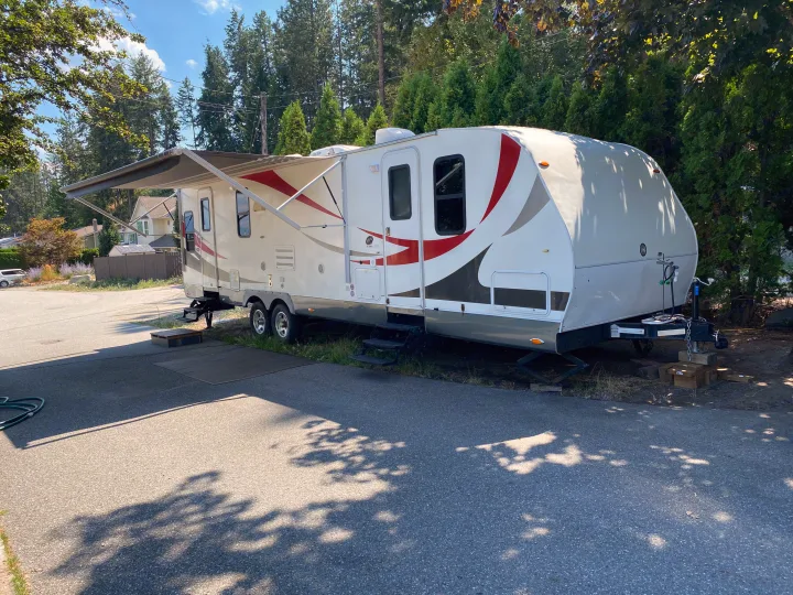 White RV rental travel trailer with an extended awning, parked on asphalt under a sunny sky.. MVP Coast 2009