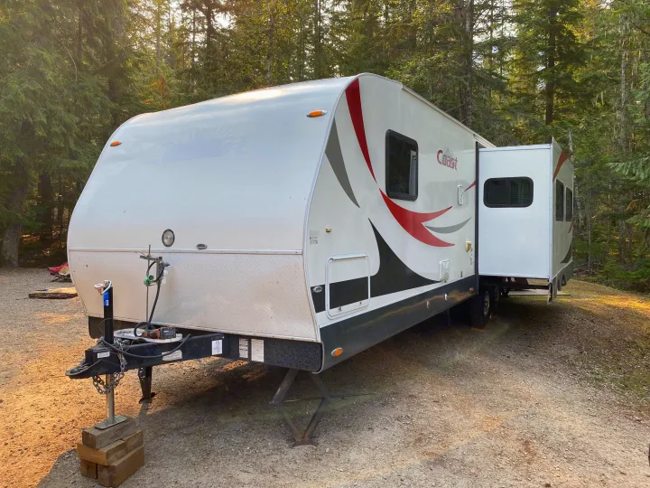 Experience nature in comfort! This white travel trailer RV rental, featuring a slide-out, is ready at a wooded campsite.. MVP Coast 2009