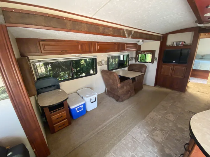 Interior of an RV rental showing living area with dinette, entertainment center, kitchen storage, and bedroom beyond.. MVP Coast 2009