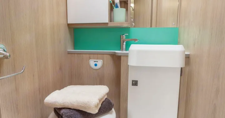 Modern compact bathroom in an RV rental, with a sink, toilet, and wood-grain interior.. Auto-Trail F74 2025