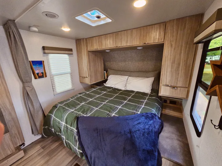 Experience comfortable travel in this RV rental's bedroom, complete with plaid bedding, storage, and natural light.. Winnebago Minnie 2201MB 2022
