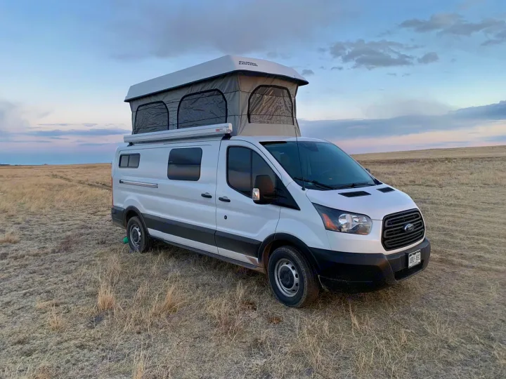 White camper van with pop-top tent in a dry field under cloudy skies, perfect for an RV rental getaway.. Ford Transit Custom 2019