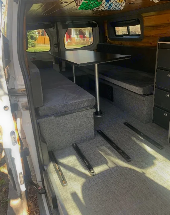 RV rental: Modular camper van interior with grey bench seating, table, floor tracks, and wood ceiling. Versatile for travel.. Ford Transit Custom 2019