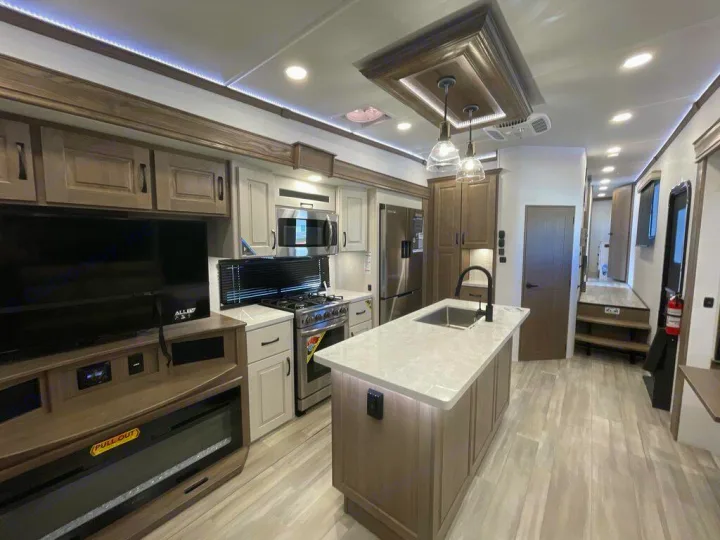 Spacious RV rental interior with modern kitchen island, stainless appliances, and living area with TV/fireplace.. Alliance RV Paradigm 2024