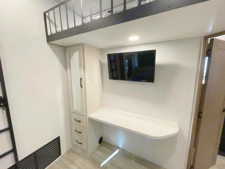 RV rental interior: loft bed, desk, wall-mounted TV, & built-in storage cabinet.. Alliance RV Paradigm 2024