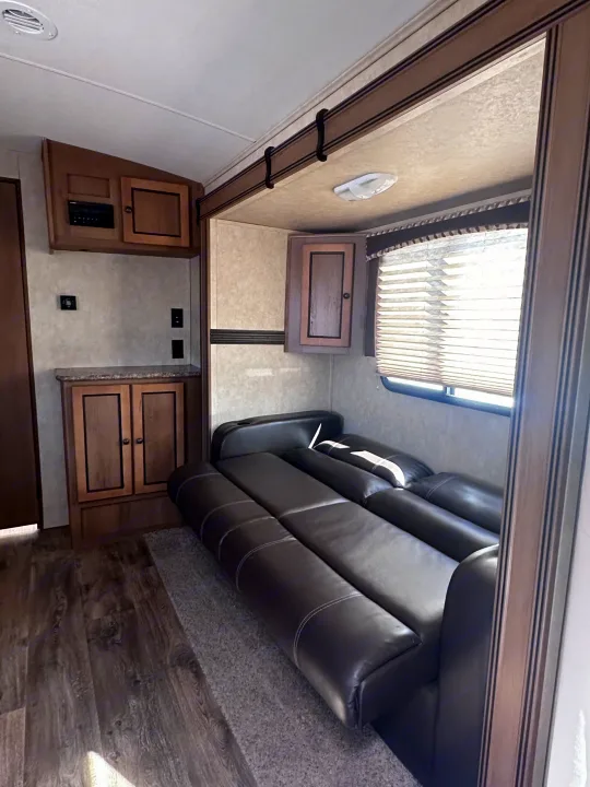 Inside this RV rental: a dark leather sofa-bed, wood cabinets with an entertainment system, and a window with blinds.. Cruiser RV Shadow Cruiser 2016
