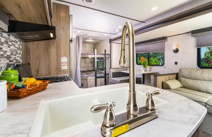 Explore this modern RV rental's cozy interior, featuring a full kitchen with sink, bunk beds, dining area, and living space.. Gulf Stream Ameri-Lite 2024