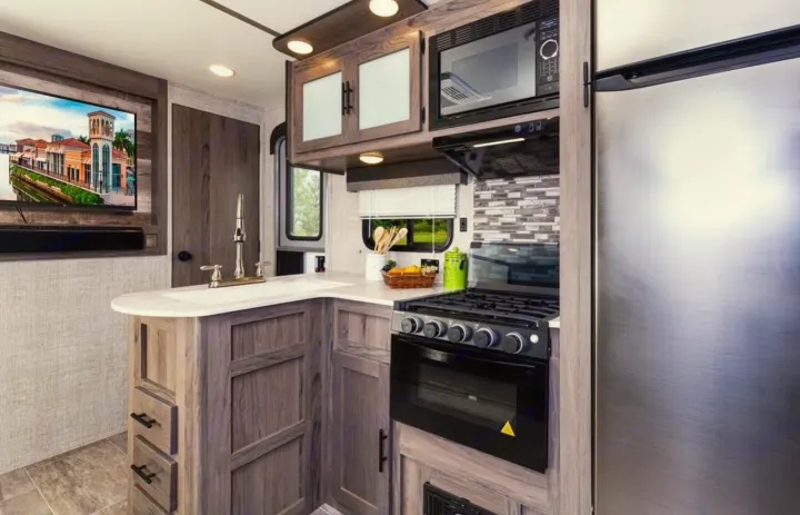 Modern RV rental interior with a full kitchen (stove, microwave, fridge), counter space, and TV area.. Gulf Stream Ameri-Lite 2024