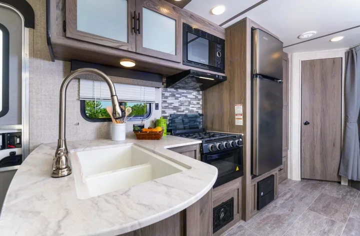 Modern RV rental kitchen with stainless appliances: sink, microwave, oven, and fridge. Wood cabinetry & countertop shown.. Gulf Stream Ameri-Lite 2024
